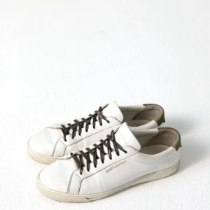 Vita sneakers från Saint Laurent - Vi säljer ett par otroligt unika och exklusiva Saint Laurent skor i vit läder med cammo snören! Storleken är 43 1/2! Nypris på dessa ligger på ca 7000kr, och vårat utropspris ligger på 2000kr