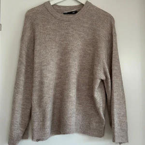 Beige stickad tröja från 157 - Mysig beige stickad tröja från 157 med rund halsringning och långa ärmar. Perfekt för lager-på-lager och enkel att matcha med olika outfits. Klassisk och stilren design.