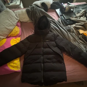 Svart pufferjacka från Sail Racing - Säljer en svart pufferjacka från Sail Racing i storlek medium. Jackan har huva, dragkedja framtill och är tillverkad med Primaloft-foder för extra värme. Vattentät och andas, perfekt för kalla dagar. Snygg och stilren design med Sail Racing-logga på bröstet. Den är helt oanvänd 