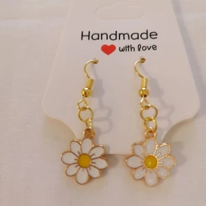 Handgjorda örhängen med prästkrage - Säljer ett par söta handgjorda örhängen i form av prästkragar. Blommorna har vita kronblad och en gul mitt, med guldfärgade detaljer och krokar. Perfekta för att ge en lekfull touch till din stil.