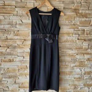 Svart klänning med rosett från H&M - Snygg svart ärmlös klänning från H&M med v-ringning och dekorativ rosett i midjan. Klänningen har en markerad midja och rak passform, perfekt för en stilren look.