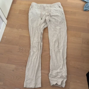 Beiga linnebyxor från Dressmann - Säljer ett par beiga linnebyxor från Dressmann i storlek XS. Byxorna har dragsko i midjan och elastisk resår för extra komfort. Perfekta för varma dagar med sin lätta och luftiga känsla.