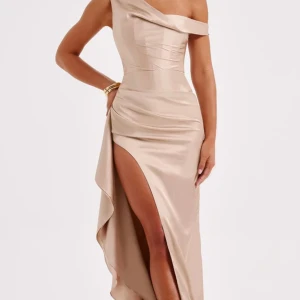 Champagnefärgad balklänning med slits från Babyboo  - Säljer en elegant, champagnefärgad balklänning från babyboo fashion. Klänningen har en asymmetrisk one shoulder-design, hög slits och vackra draperade detaljer. Tillverkad i glansigt satinmaterial som ger en lyxig känsla. Spliterny med prislapp kvar och i orginalförpackning. Pris går att diskuteras.