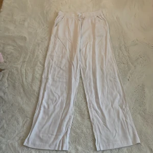 Vita vida byxor med resårmidja - Säljer ett par vita linne byxor med resår i midjan och raka, vida ben. Byxorna har fickor på sidorna och en bakficka. Perfekta för en avslappnad stil och tillverkade i ett lätt material.