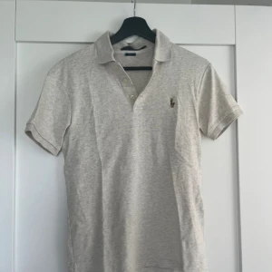 Beige pikétröja från Polo Ralph Lauren - Säljer en klassisk beige pikétröja från Polo Ralph Lauren med broderad logga på bröstet. Tröjan har korta ärmar, krage och knappar framtill. Slim fit-modell som sitter snyggt och stilrent. Skick 9/10 Hör av dig vid frågor! Nypris 1300 mitt pris 370 (kan diskuteras vid snabb affär!)