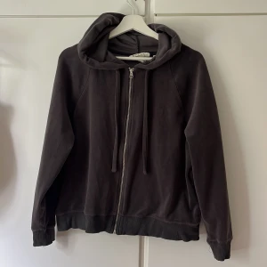 Mörkgrå hoodie med dragkedja - Säljer en mörkgrå hoodie med dragkedja framtill och huva med snören. Tröjan har långa ärmar och ribbade muddar vid ärmslut och nederkant. Supermjukt och mysigt material.