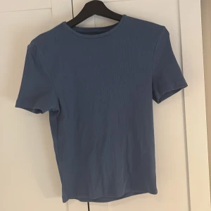 Blå ribbad t-shirt från BikBok - Säljer en enkel och stilren blå ribbad t-shirt från BikBok. T-shirten har rund halsringning och korta ärmar, perfekt för en avslappnad look. Passar till det mesta och är superbekväm att bära. Tyvärr lite för stor för mig så hoppas någon annan får användning av den istället!💕