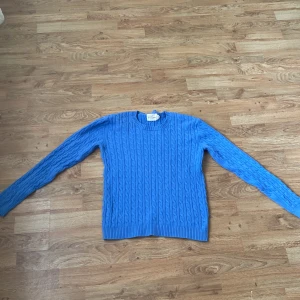 Blå kabelstickad tröja från Holly & Whyte - Snygg blå kabelstickad tröja från Holly & Whyte. Tröjan har rund halsringning och långa ärmar. Perfekt för lager-på-lager och passar till många olika stilar.