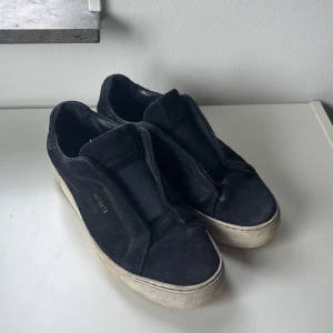 Axel Arigato - Mörkblå sneakers från Axel Arigato med ovandel i mocka och bred resår över vristen istället för klassisk snörning. Skorna har en vit, platt sula och en stilren, minimalistisk design. Perfekta för dig som gillar enkel och clean stil. Skriv vid minsta funderingar🙌