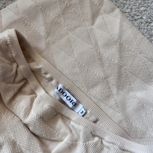 Beige klänning från Adoore - Säljer en beige långklänning från Adoore i storlek 38. Klänningen är axelbandslös med diskret strukturmönster och har en slits baktill. Har extra tyg över bröstet och är ganska tjock i tyget. Säljer pga att jag aldrig använt den.