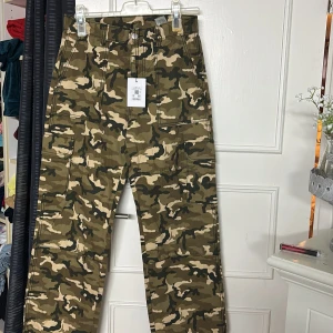 Cargobyxor i camouflage - Säljer ett par cargobyxor i klassiskt camouflage-mönster med flera fickor på sidorna. Byxorna har normal passform och är perfekta för en avslappnad streetstil. Stängs med dragkedja och knapp i midjan.