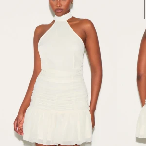 Vit halterneck klänning från Bershka - Säljer en vit kortklänning från prettylittlething med halterneck och markerad midja. Klänningen har rynkade detaljer längs sidorna och en lätt volang nedtill. Perfekt nu till sommaren. Den är helt ny med lapp på. Den är i storlek 10 (M).