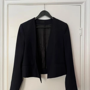 Svart kavaj från Filippa K - Säljer en stilren svart kavaj från Filippa K i storlek medium. Kavajen är croppad med lång ärm och har en enkel, öppen front utan knappar. Perfekt för en clean och modern look.