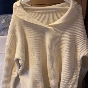 Krämvit stickad tröja med v-ringning - Mysig krämvit stickad tröja med bred v-ringning och avslappnad passform. Perfekt för lager-på-lager och passar till många olika stilar. Ribbad struktur i materialet ger en extra touch.