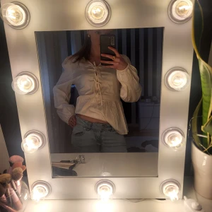 Vit blus med knytband - Säljer en söt vit blus med rosetter framtill. Blusen har långa ärmar och en lätt volang nertill som ger en romantisk känsla. Perfekt att matcha med jeans eller kjol för en trendig look.