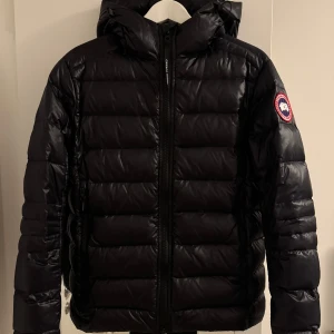 Canada Goose Jacka - Jätte fin stilren sällsynt Canada Goose dunjacka mörkblå/svart. Jackan har klassisk logotyp på ärmen och quiltad design. Passar alla tillfällen den är som ny medkommer en rem också hör av er för fler bilder, pris kan diskuteras vid snabb affär.