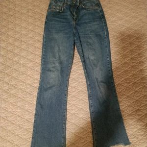 Blå jeans med rå kant - Säljer ett par blå jeans med raka ben och rå, fransig kant längst ner. Klassisk femficksmodell med normal passform och hög midja. Perfekta för en avslappnad och trendig look.