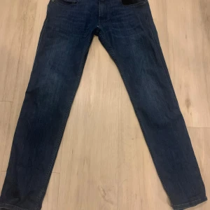 Mörkblå Replay Anbass jeans - Säljer ett par mörkblå Replay Anbass jeans med klassisk femficksdesign och raka ben. Jeansen har snygga detaljer vid fickorna . Har väldigt bra passform och är i bra skick. Tveka inte att höra av er vid intresse.