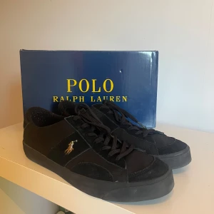 Svarta sneakers från Polo Ralph Lauren - Säljer ett par svarta sneakers från Polo Ralph Lauren med klassisk logga på sidan. Skorna har snörning och rund tå, samt en platt sula. Perfekta för en stilren och avslappnad look. Använda 5-6 gånger och har inga defekter. Säljer då de är för stora för mig för att jag köpte storleken för stor. Jag är öppen för byten. Nypris 1200. Mitt pris är inte huggigt i sten.