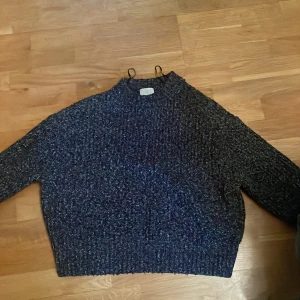 Mörkgrå stickad tröja från H&M - Mysig mörkgrå stickad tröja från H&M med grovstickad struktur. Tröjan har lång ärm och en något croppad passform, perfekt för kyliga dagar. Enkel och stilren design som passar till det mesta.
