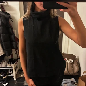 Svart ärmlös polotopp - Säljer en svart ärmlös polotopp med hög krage. Enkel och stilren modell som passar till många olika outfits. Perfekt för dig som gillar minimalistisk stil. Pris diskuterbart