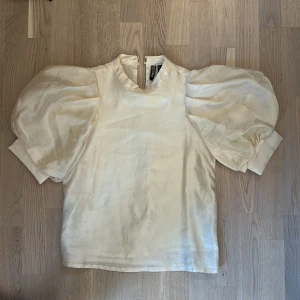 Krämvit blus med puffärmar från PIECES - Säljer en krämvit blus från PIECES med stora puffärmar. Blusen har knäppning i nacken och är tillverkad i ett glansigt material. Storlek s, köparen står för frakt🩷