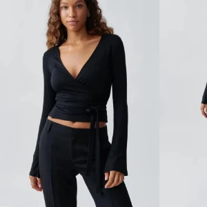 Svart omlottopp med knyt - Snygg svart omlottopp med lång ärm och djup v-ringning. Toppen har knyt i midjan som ger en smickrande passform. Perfekt att styla med både jeans och kostymbyxor.