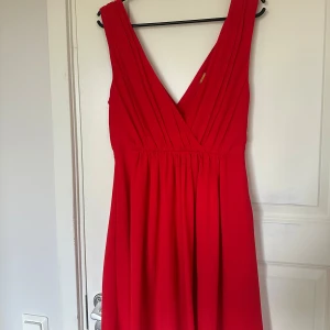Röd långklänning med djup v-ringning - Säljer en röd långklänning med djup v-ringning och breda axelband. Klänningen har ett fint fall och markerad midja, perfekt för speciella tillfällen. Materialet känns mjukt och följsamt.