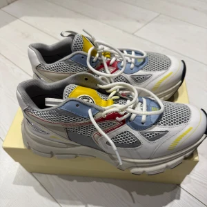 Axel Arigato Marathon Runner sneakers i vitt, blått och gult - Säljer ett par snygga Axel Arigato sneakers i vitt med detaljer i blått, gult och rött. Skorna har meshpaneler för extra ventilation, vita snören och en chunky sula. Knappt använda av förra ägaren och var för stora för mig. Det gula lädret har färgat av sig pyttelite på skosnöret, annars ingen anmärkning. Känns mera som en storlek 41.