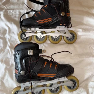 Svarta inlines från Soc med orange detaljer - Säljer ett par svarta inlines från Soc med orangea och grå detaljer. Skorna har snörning, spänne och kardborreband för extra stabilitet. Hårda hjul och robust konstruktion, perfekt för dig som gillar fart och rörelse.