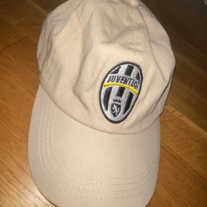 Beige Juventus keps - Snygg beige keps med Juventus-logga broderad framtill. Justerbar rem baktill för perfekt passform. Perfekt för dig som vill visa ditt stöd för Juventus på ett stilrent sätt.