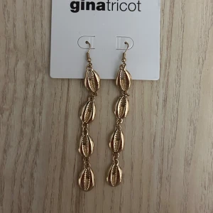 Guldiga snäckformade örhängen - Långa, hängande örhängen i guldmetall med fyra snäckformade länkar på rad. Perfekta för att ge en strandig och trendig touch till din look. Örhängeskortet är lite slitet men örhängena är helt oanvända, inte ens prövats.