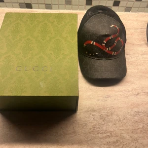 Svart keps från Gucci med ormtryck - Gucci Keps Storlek M/58. Säljer kepsen efter att ha bytat klädstil. Kvitto finns inte men köpt från Guccis hemsida för ca 4000. 