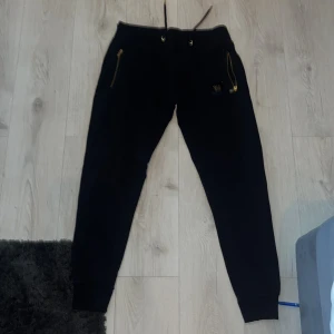 Svarta mjukisbyxor från MR Originals - Svarta mjukisbyxor från MR Originals med guldfärgade dragkedjor på fickorna och guldfärgad logga på ena benet. Köpta från kicksnstuff i Göteborg 2022 lite små i storleken men passar mig som är 185 fortfarande men är lite korta