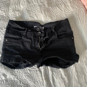Svarta jeansshorts med dragkedjor - Svarta jeansshorts med råa kanter och dubbla knappar fram. Shortsen har fickor både fram och bak, samt snygga dragkedjor på bakfickorna. Perfekta för sommaren och passar till det mesta.