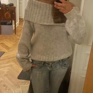 Ljusgrå offshoulder stickad tröja - Mysig ljusgrå stickad tröja med bred offshoulder-krage. Tröjan har lång ärm och en avslappnad passform, perfekt för kyliga dagar. Snygg att styla med jeans eller kjol.