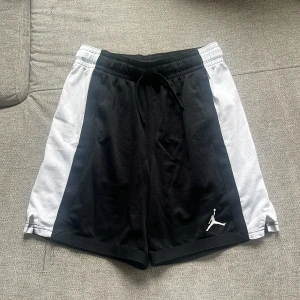 Svarta och vita Jordan shorts med snörning - Snygga sportiga shorts från Jordan i svart med vita sidopaneler och snörning i midjan. Ikonisk Jumpman-logga på vänster ben. Perfekta för träning eller chill. Mjukt och lätt material. Dom är använda fåtal gånger och inga skador 