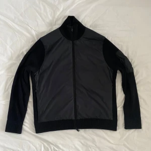 Svart hybridjacka från J.Lindeberg - Säljer en svart hybridjacka från J.Lindeberg som är knappt använd. Den har inga defekter eller fläckar. Original pris 3300, fastsatt pris kan förhandlas