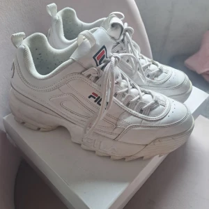 Vita sneakers från Fila - Säljer ett par chunky vita sneakers från Fila med klassisk logga på sidan, plös och häl. 👟💓💓Skorna har snörning och en rejäl platt sula som ger extra höjd. I någorlunda fint skick och är i storlek 41. Har ej kvar orginalkartongen så får fraktas på annat sätt.😊