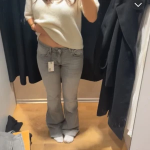 Ljusgrå bootcut jeans - Säljer ett par ljusgrå jeans med bootcut passform och klassiska fem fickor. Jeansen är lågmidjade och stängs med dragkedja och knapp. Perfekta för dig som gillar en retroinspirerad look.
