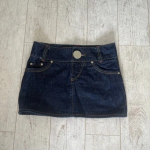 Mörkblå lågmidjad jeanskjol  - Snygg mörkblå jeanskjol från MP Jeans med klassiska fickor fram och bak, bred linning och stor silverfärgad knapp. Tuff kontrastsöm i gult och rött ger extra edge. Perfekt till sneakers eller boots för en cool look.Midjemått 38 cm Längd 31 Skulle säga att det är storlek xs-s