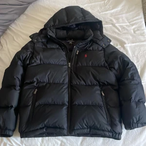 Svart pufferjacka från Polo Ralph Lauren - Säljer en svart vinterjacka från Polo Ralph Lauren i storlek S. Jackan har huva, dragkedja framtill och två sidofickor med dragkedja. Klassisk design med Polo-logga i rött på bröstet. Använt den fåtal gånger så skicket är väldigt bra🌟👍