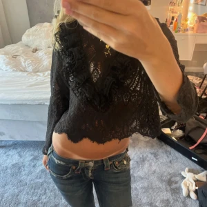 Svart spetsig croppad blus från Zara - Säljer en svart croppad blus i spets med långa ärmar och fina volangdetaljer. Blusen har ett genombrutet mönster och vågig kant nertill, perfekt som fest topp från Zara endast testad💗