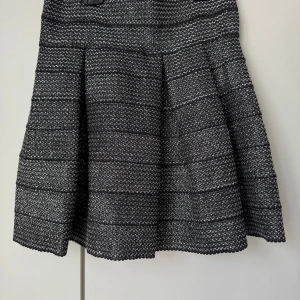 Svart och grå kortkjol med struktur - Snygg kortkjol i svart och grått med strukturerat tyg och subtila horisontella ränder. Kjolen har en lätt utställd form som ger en cool siluett och passar perfekt till en stickad tröja eller skinnjacka.