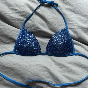 Blå glittrig bikini från Calzedonia - Supersnygg blå trekantsbikini från Calzedonia med massor av glittrande paljetter på framsidan. Klassisk modell med knyt i nacken och ryggen. Perfekt för dig som vill sticka ut på stranden i sommar! Materialet är mjukt och stretchigt syntet. Storlek S!💗