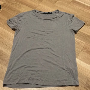 Grå basic t-shirt från 157 - En enkel grå t-shirt från 157 i storlek S. Modellen är klassisk med rund hals och korta ärmar, perfekt för en chill och avslappnad stil. Materialet känns mjukt och skönt mot huden, och färgen är neutral vilket gör den lätt att matcha med allt.