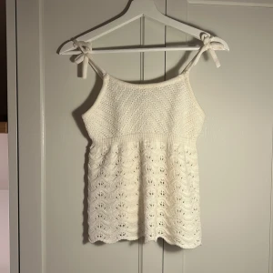 Vit stickad linnetopp Freshman - Supersöt vit stickad linnetopp från Freshman med knytbara axelband och vågig spetsstickad nederdel. Toppen har en luftig och romantisk känsla, perfekt för varma dagar. Snyggt mönster och mjukt material som känns skönt mot huden.