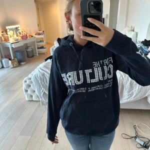 Mörkblå hoodie med tryck - Säljer en mörkblå hoodie med vit text och grafiskt tryck på bröstet och ärmen. Tröjan har huva med snörning och en stor magficka framtill. Jätte bekvämt och lätt tyg. Aldrig använd. 