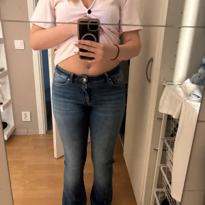 Blå bootcut jeans med låg midja - Säljer ett par snygga blå jeans med bootcut-modell och låg midja. Jeansen har klassisk femficksdesign, lätt slitning framtill och är tillverkade i stretchigt denim för en bekväm passform. Perfekta för dig som gillar en tidlös och avslappnad look.