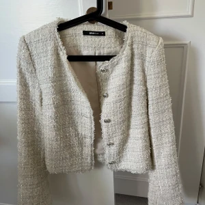 Beige kavajjacka från Gina Tricot - Snygg beige kavajjacka från Gina Tricot i strukturerat, tweed-liknande material. Jackan har rund halsringning, långa ärmar och silverfärgade knappar framtill. Nästan helt oanvänd!